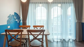 Een eethoek met een tafel en stoelen, een wand met blauwe accenten en een raam met gordijnen.
