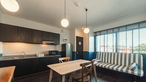 Een moderne keuken met donkere kastjes, een houten eettafel en een gestreepte bank bij een groot raam.