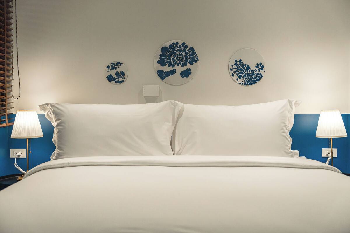 Ein Bett mit weißer Bettwäsche, zwei Nachttischlampen und drei floral dekorierte Wandbilder.