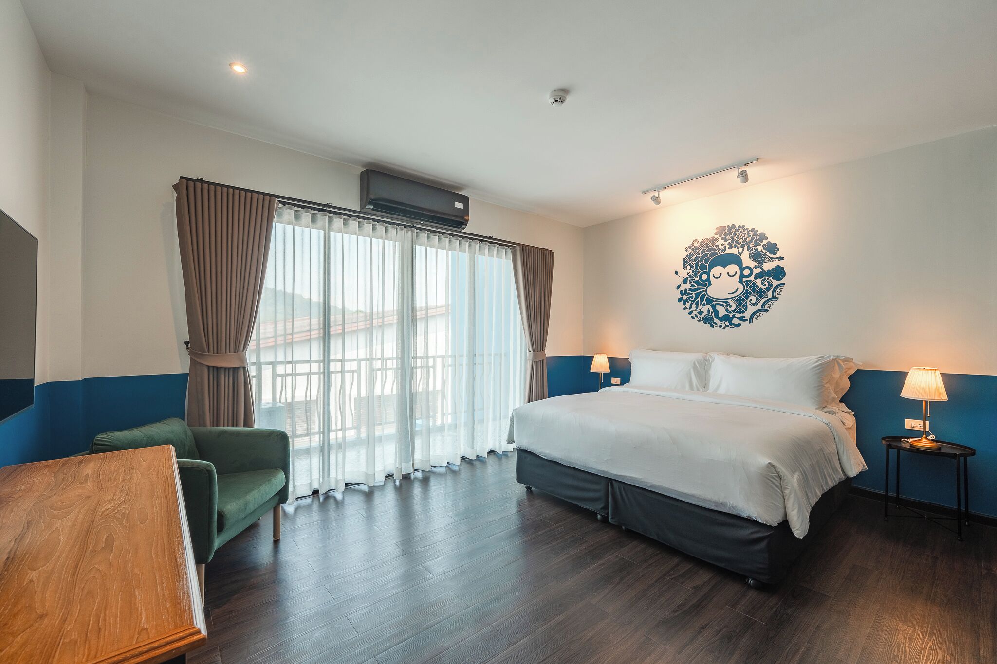 Habitación de hotel con cama, escritorio, silla, un adorno en la pared y ventana con cortinas.