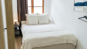 A neatly made bed with a white comforter and pillows, a bedside table with a lamp, and a window with curtains. - Modern 3BR Apt for 6 with Patio Ghent (Ghent)