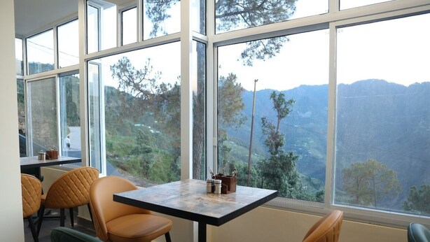 Un espace repas comprenant une table et des chaises, de grandes fenêtres offrant une vue sur les montagnes et sur le paysage environnant.