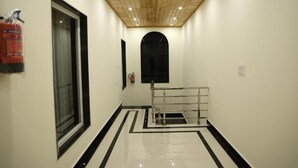 Un couloir avec un plafond en bois, un extincteur fixé au mur, une fenêtre à cadre noir et une rambarde métallique au centre.