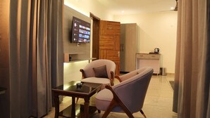 Une chambre d’hôtel moderne dotée d’un téléviseur à écran plat fixé au mur, d’une armoire en bois, d’une petite kitchenette et d’un coin salon avec une table et deux chaises.