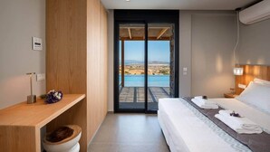A modern hotel room with a bed, bedside table, and a view of a pool and landscape. - Vista Blue Villa Naxos - 2 (Τοπική Κοινότητα Βίβλου)