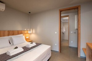 Ein Hotelzimmer mit Bett, Nachttischen, einer Wand-Klimaanlage und einer Tür zu einem Badezimmer.
