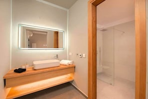 Ein modernes Badezimmer mit einem großen Spiegel, einer Holzausstattung, einem weißen Waschbecken und einer Duschkabine aus Glas.