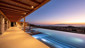 A infinity pool with a view of the landscape and a covered seating area with lounge chairs. - Vista Blue Villas Naxos | 16 Guests (Τοπική Κοινότητα Βίβλου)