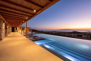 A infinity pool with a view of the landscape and a covered seating area with lounge chairs. - Vista Blue Villas Naxos | 16 Guests (Τοπική Κοινότητα Βίβλου)