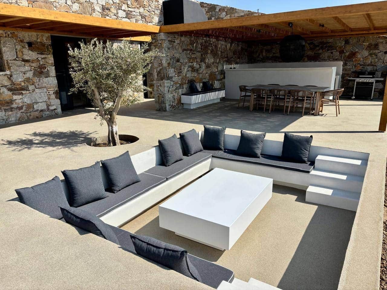 A modern outdoor seating area with a stone wall, a white table, and a barbecue grill.