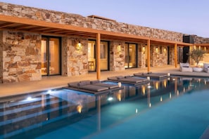 A modern outdoor pool area with stone walls, lounge chairs, and a clear blue pool. - Vista Blue Villa Naxos - 1 (Τοπική Κοινότητα Βίβλου)