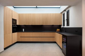 A modern kitchen with wooden cabinetry, a black countertop, and a built-in dishwasher. - Vista Blue Villa Naxos - 1 (Τοπική Κοινότητα Βίβλου)