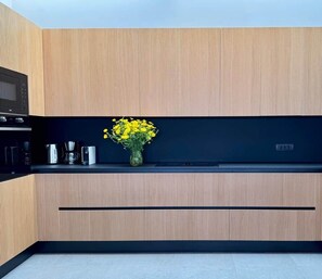 A modern kitchen with a wooden panel wall, a black countertop, and a vase with yellow flowers. - Vista Blue Villa Naxos | Luxury for Two (Τοπική Κοινότητα Βίβλου)