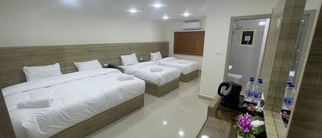 Habitación de hotel con tres camas, cabecera de madera, espejo, cafetera y dispensador de agua.