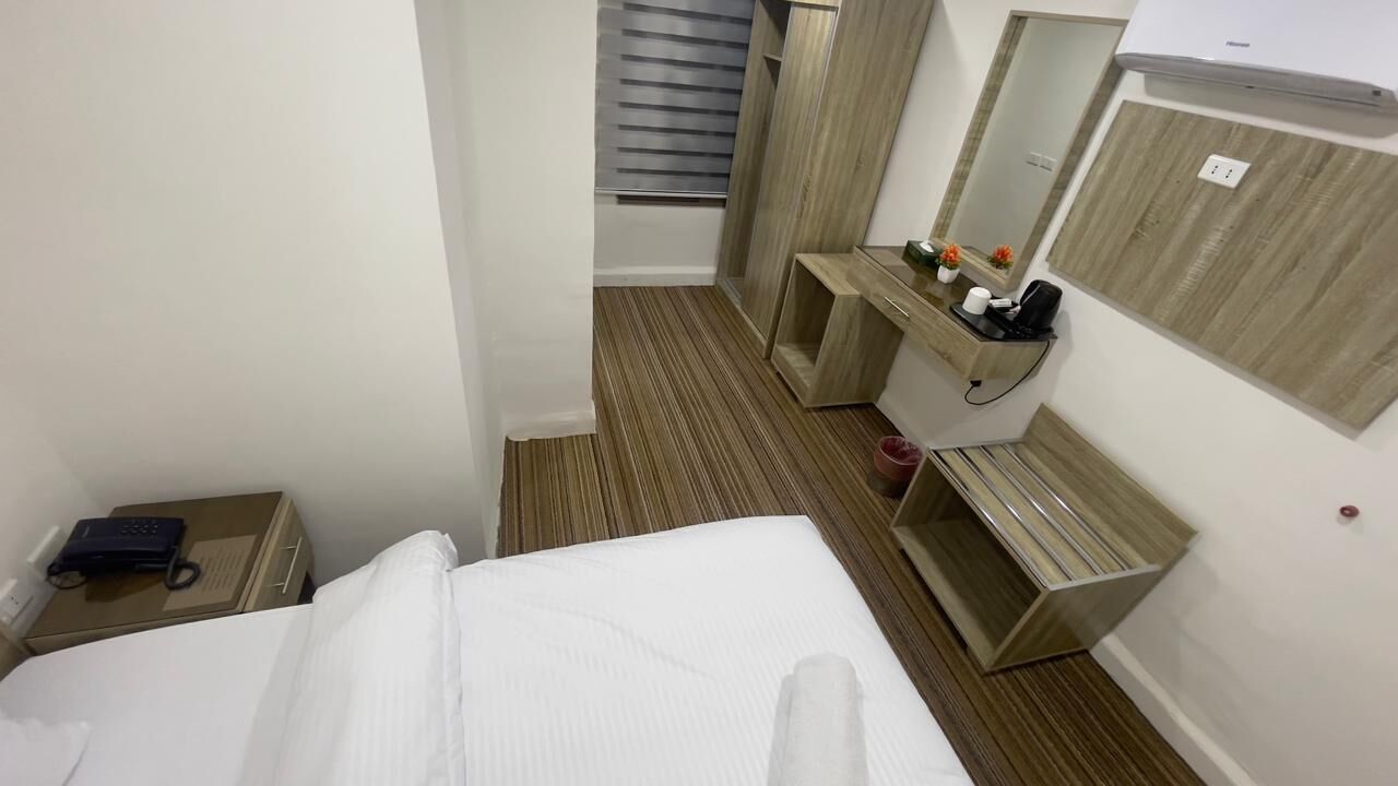 A hotel room with a bed, a desk, a mirror, and a wardrobe.