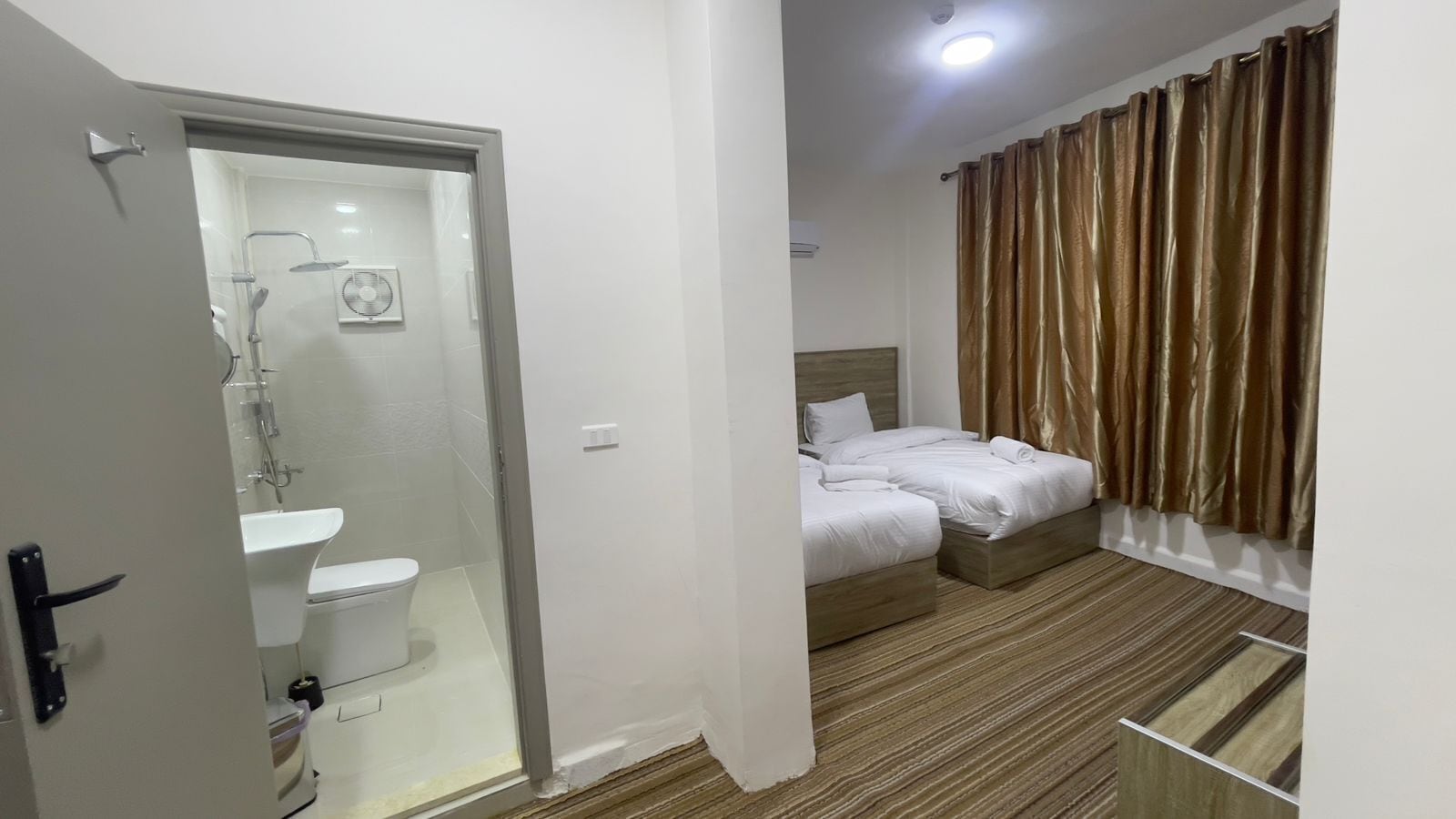 A hotel room with a shower area, a bed, and a window with curtains.