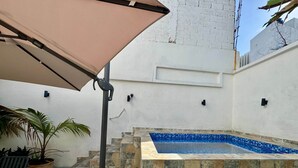 A pool area with stone steps leading to a blue-tiled pool, a pergola with a beige canopy, and potted plants. - Colonial Home with Private Terrace and Jacuzzi (Santo Domingo)