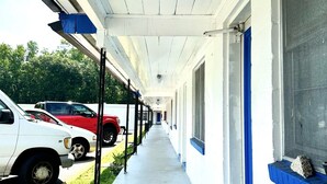 A covered corridor with a row of parked cars on one side and a building with blue trim on the other. - Soho Inn Waldo (Waldo)