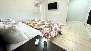 Une chambre d’hôtel avec un lit, un téléviseur fixé au mur, une télécommande posée sur une table et une porte donnant sur une autre pièce.