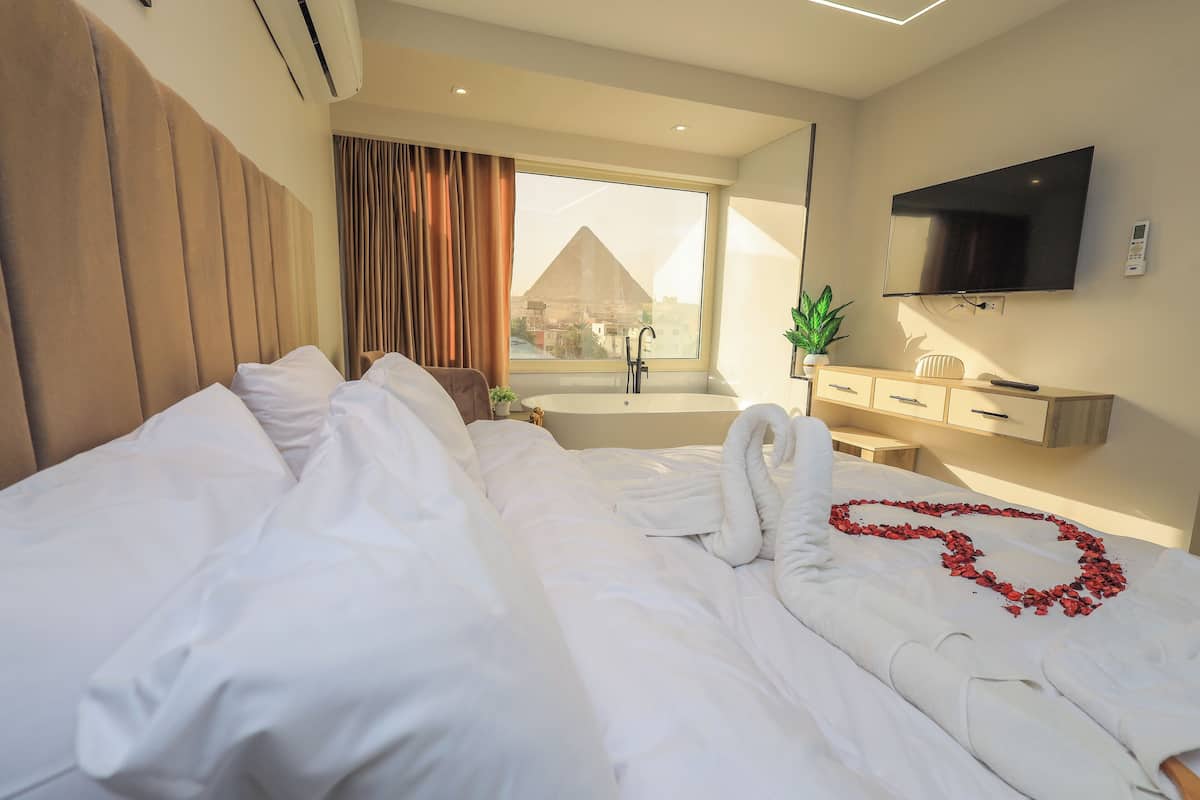 Camera d'albergo con un grande letto, una TV, una finestra con vista su una piramide e una vasca da bagno.