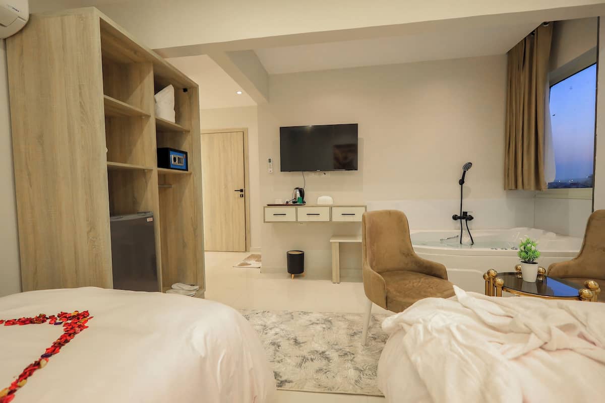 Camera d'albergo con due letti, una scrivania, un televisore, una vasca da bagno e un piccolo tavolino con una pianta.