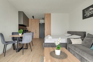 Un ambiente compatto con angolo cottura, zona pranzo con tavolo e sedie, divano e un letto.