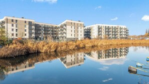 Un moderno complejo de apartamentos con varios pisos y balcones, reflejado en una superficie acuática tranquila.