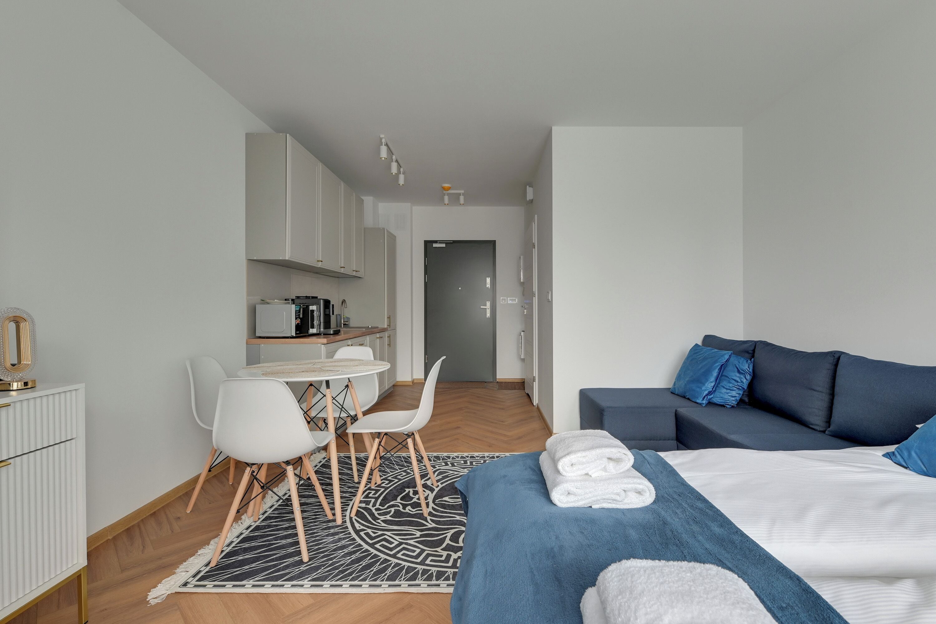 A modern hotel room with a bed, a sofa, a dining area, and a kitchen.