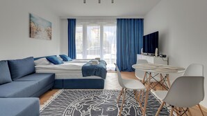 Una habitación de hotel moderna con cama, sofá, mesa de comedor, sillas y televisor.
