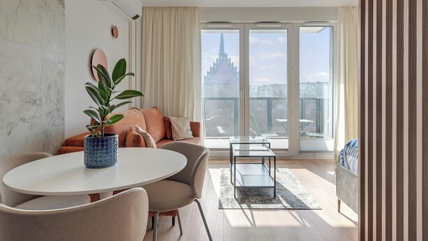 Una sala moderna con una mesa redonda, sofá y un ventanal con vistas a un paisaje urbano.