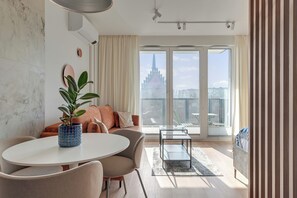 A modern living room with a round table, sofa, and a large window with a view of a cityscape. - RentPlanet - Apartamenty Portovo (Gdańsk)