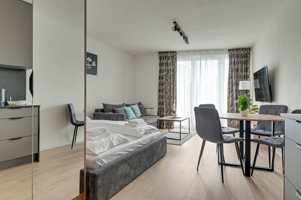 Et moderne hotelværelse med seng, skrivebord, stole, fjernsyn og et vindue med gardiner.