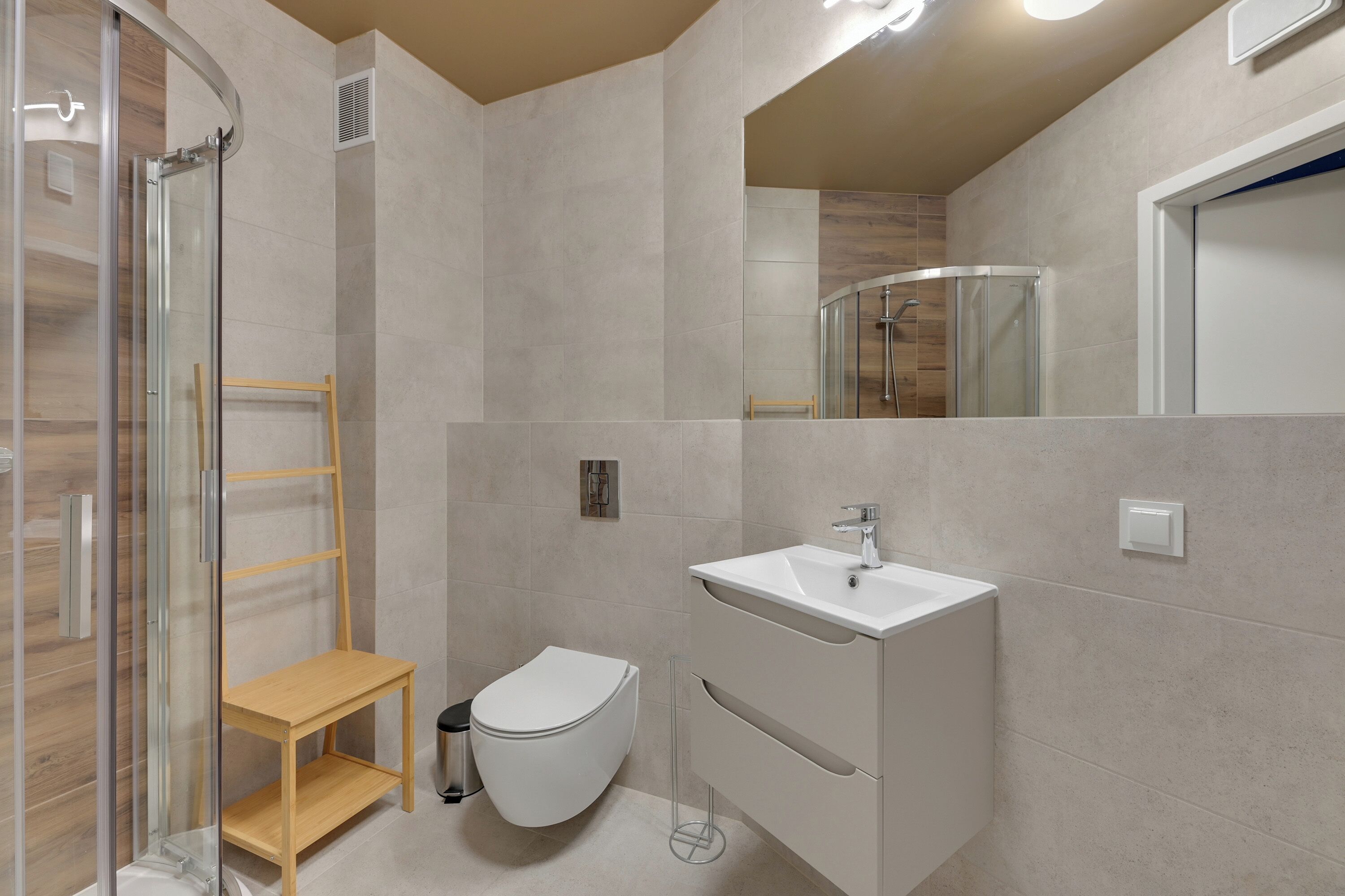 A modern bathroom with a glass shower enclosure, a wooden shelf, a white toilet, and a vanity with a sink.
