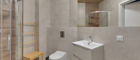 A modern bathroom with a glass shower enclosure, a wooden shelf, a white toilet, and a vanity with a sink.