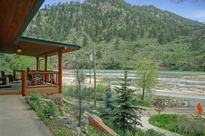 Eine Holzhütte mit Veranda, mit Blick auf einen Fluss und bewaldete Berge.
