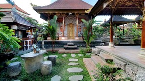 A traditional Balinese temple with a central golden gate, surrounded by stone steps, palm trees, and a garden with stone seating. - Tri Datu Palace (Sukawati)