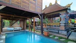 A pool area with a wooden deck, a covered seating area, and a traditional structure with ornate decorations. - Tri Datu Palace (Sukawati)