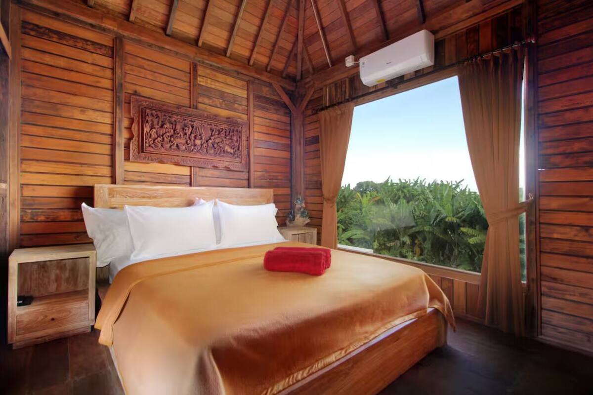 A wooden room with a bed, a nightstand, and a window with curtains.
