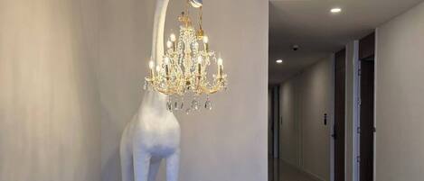 Un interior moderno con una escultura única de una jirafa que lleva un candelabro en la cabeza, un pasillo con puertas y un suelo de madera.