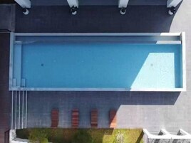 A modern building with a rectangular swimming pool, a covered outdoor seating area, and a brick wall with windows.