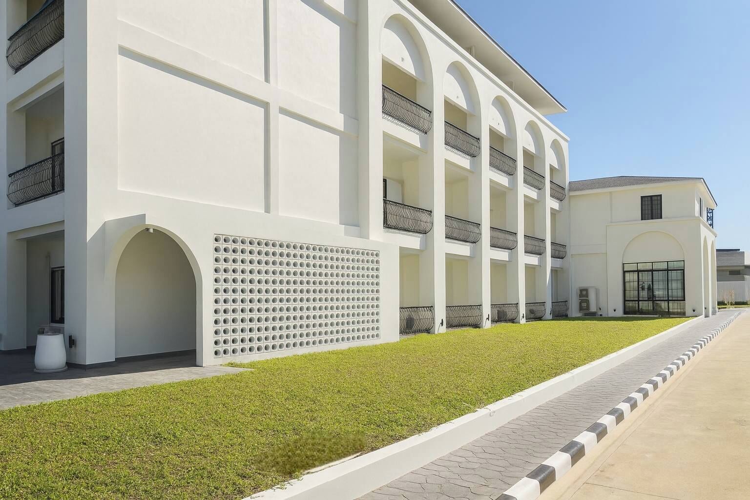 Edifici modern amb façana blanca, múltiples balcons i un jardí ben cuidat.