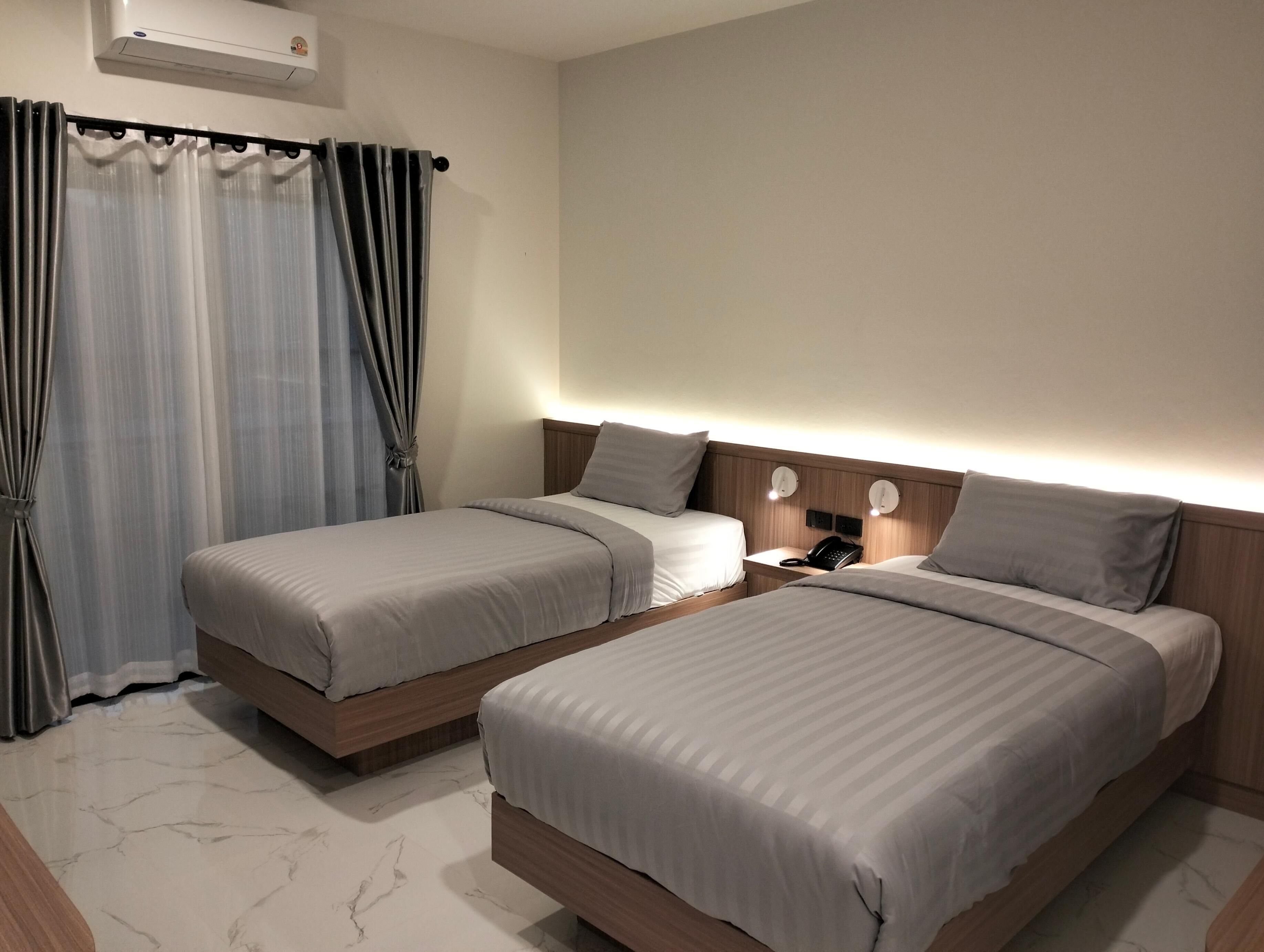 A hotel room with two beds, a nightstand with a phone, and a wall-mounted air conditioner.