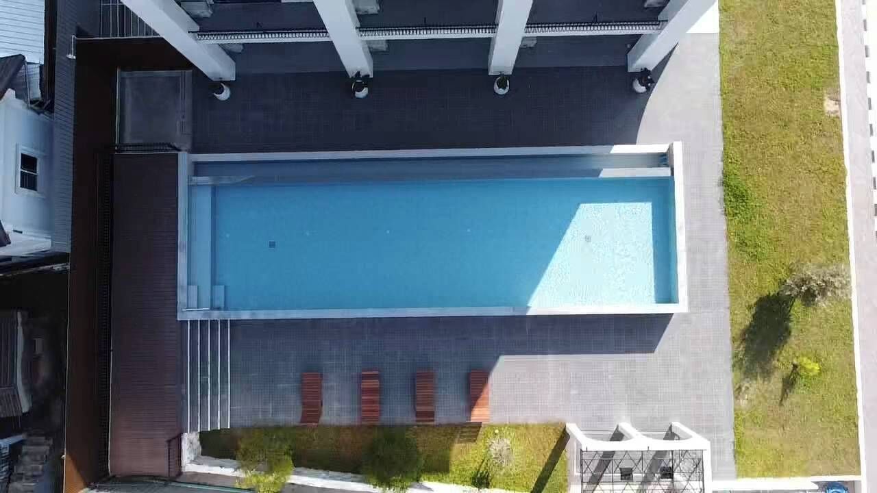 Vista aérea de un edificio moderno con piscina rectangular, un patio cubierto y un pequeño jardín con césped y algunos árboles.