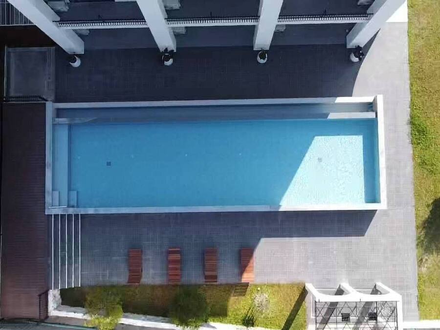 Vista aérea de un edificio moderno con piscina rectangular, un patio cubierto y un pequeño jardín con césped y algunos árboles.