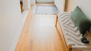 Ein Korridor mit Holzboden, einer Tür mit Blick nach draußen, einer Bank mit Sitzfläche aus Gewebe und einem wandmontierten Spiegel.