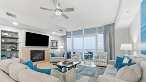 A spacious living room with a fireplace, comfortable seating, a flat-screen TV, and large windows offering a view of the city. - Turquoise C2508 (Orange Beach)