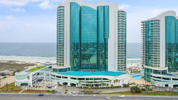 A modern hotel with a curved glass facade, multiple floors, and a pool area. - Turquoise C2508 (Orange Beach)