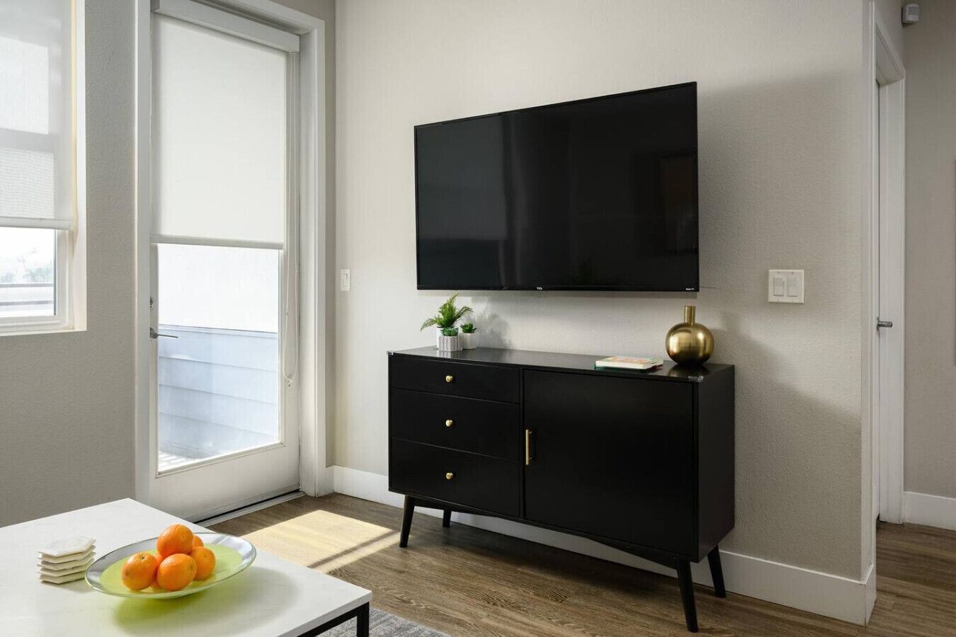 En moderne stue med et sort TV-bord, et fladskærms TV monteret over bordet, og en lille plante på bordet.