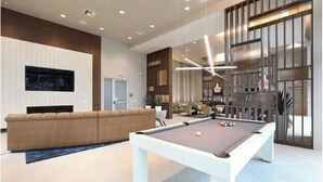 Un área interior moderna con piscina, mesa de billar, sofá y zona de estar con vista a la piscina.