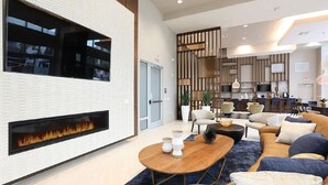 Un vestíbulo moderno con chimenea, zona de estar y una cocina al fondo.